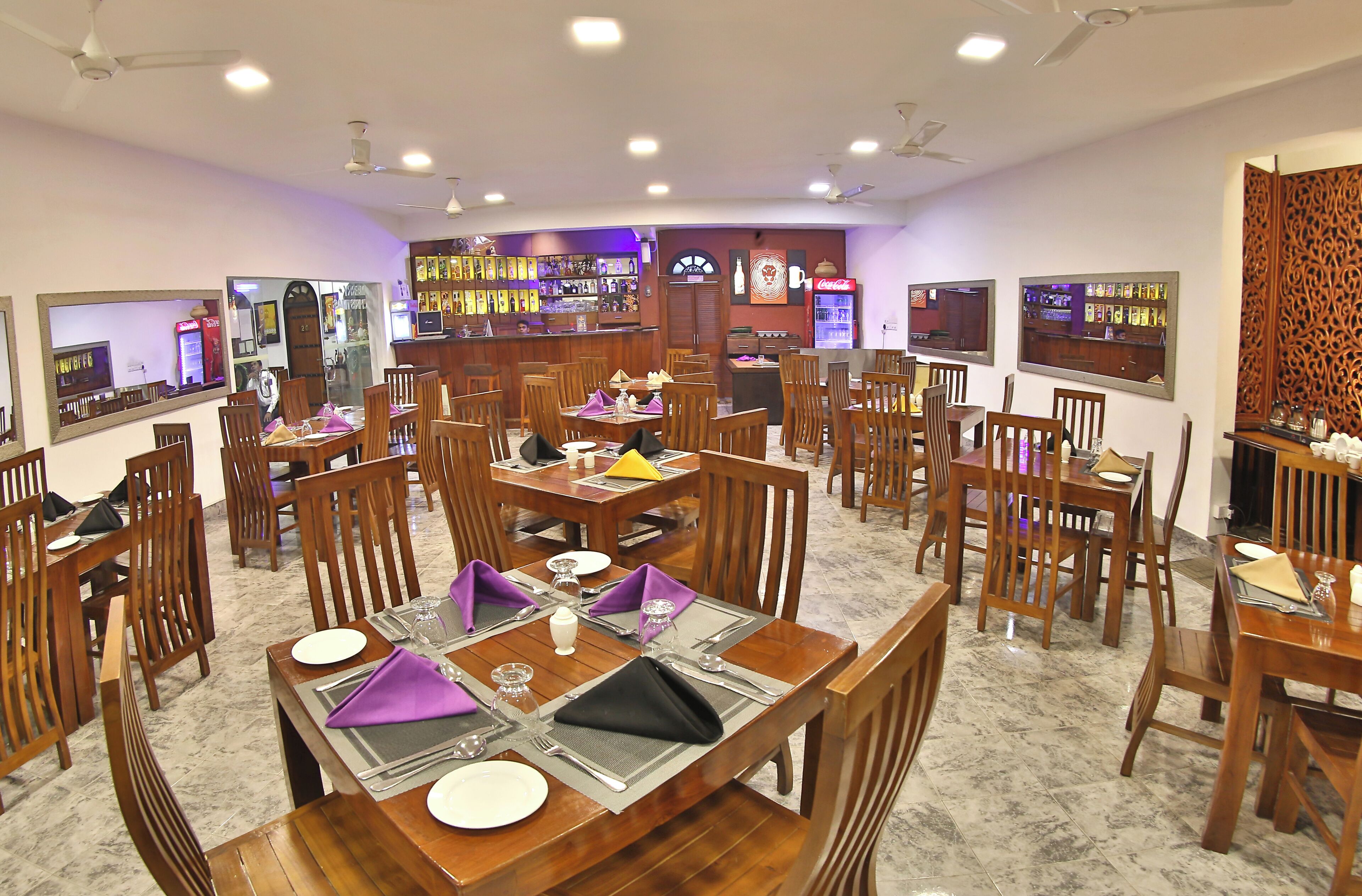 A restaurant with multiple dining tables and chairs, a bar area, and a counter with a menu display.