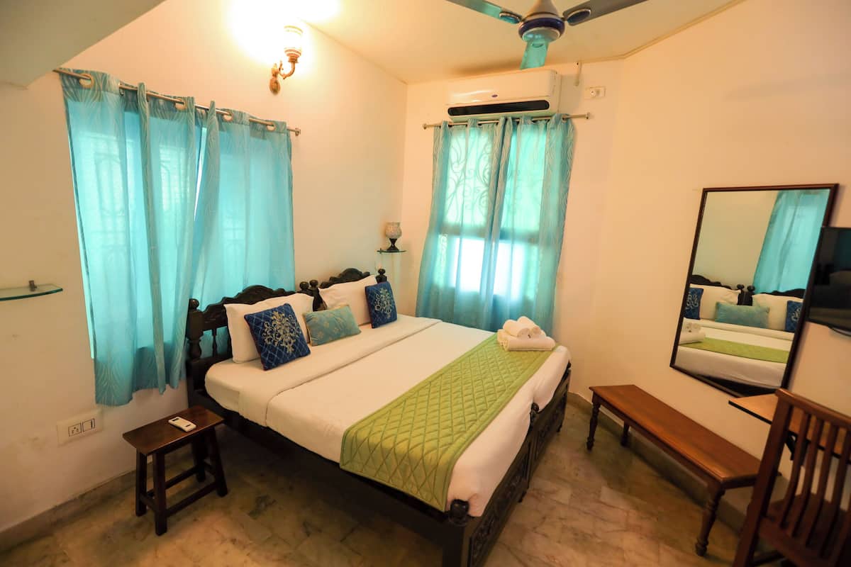 Quarto bem arrumado com cama, mesa de cabeceira, banco e ventoinha no teto.