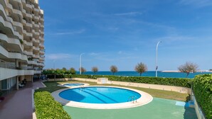 Ein Swimmingpool mit Blick auf das Meer, ein Gebäude mit Balkonen und ein klarer Himmel.