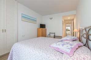 A bedroom with a bed, a dresser, a chair, a TV, and a painting on the wall.