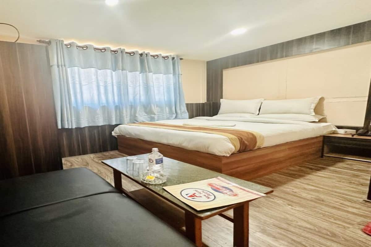 Hotellihuone, jossa on sänky, sohva, pieni pöytä, jonka päällä on pullo ja laseja, sekä kaupunkimaisemakuviolla varustettu verho.