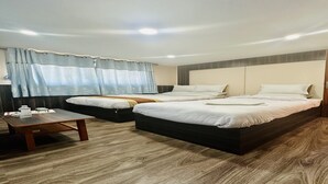 Habitación de hotel con dos camas, piso de madera, una mesita con vasos y una ventana con cortinas.