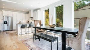 A modern kitchen with white cabinets, a stainless steel refrigerator, and a dining area with a black table and chairs. - Beach Access, Chef’s Kitchen, Rain Shower, Peloton (Camano)