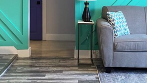 Ein Zimmer mit türkisfarbenen Wänden, einem grauen Sofa, einem kleinen Beistelltisch mit Lampe und einem Kissen mit Muster.