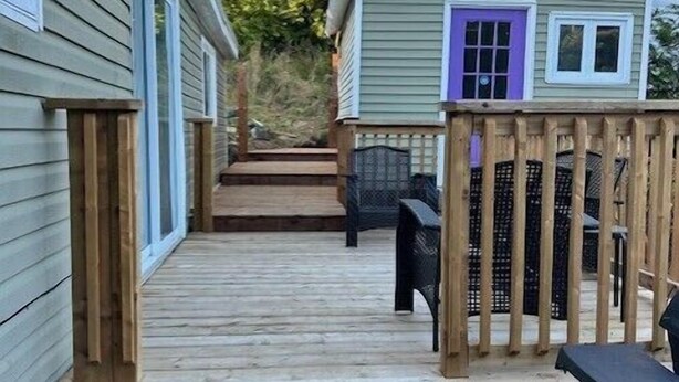 Eine Holzterrasse führt zu einem Haus mit einer violetten Tür und einem umzäunten Bereich.