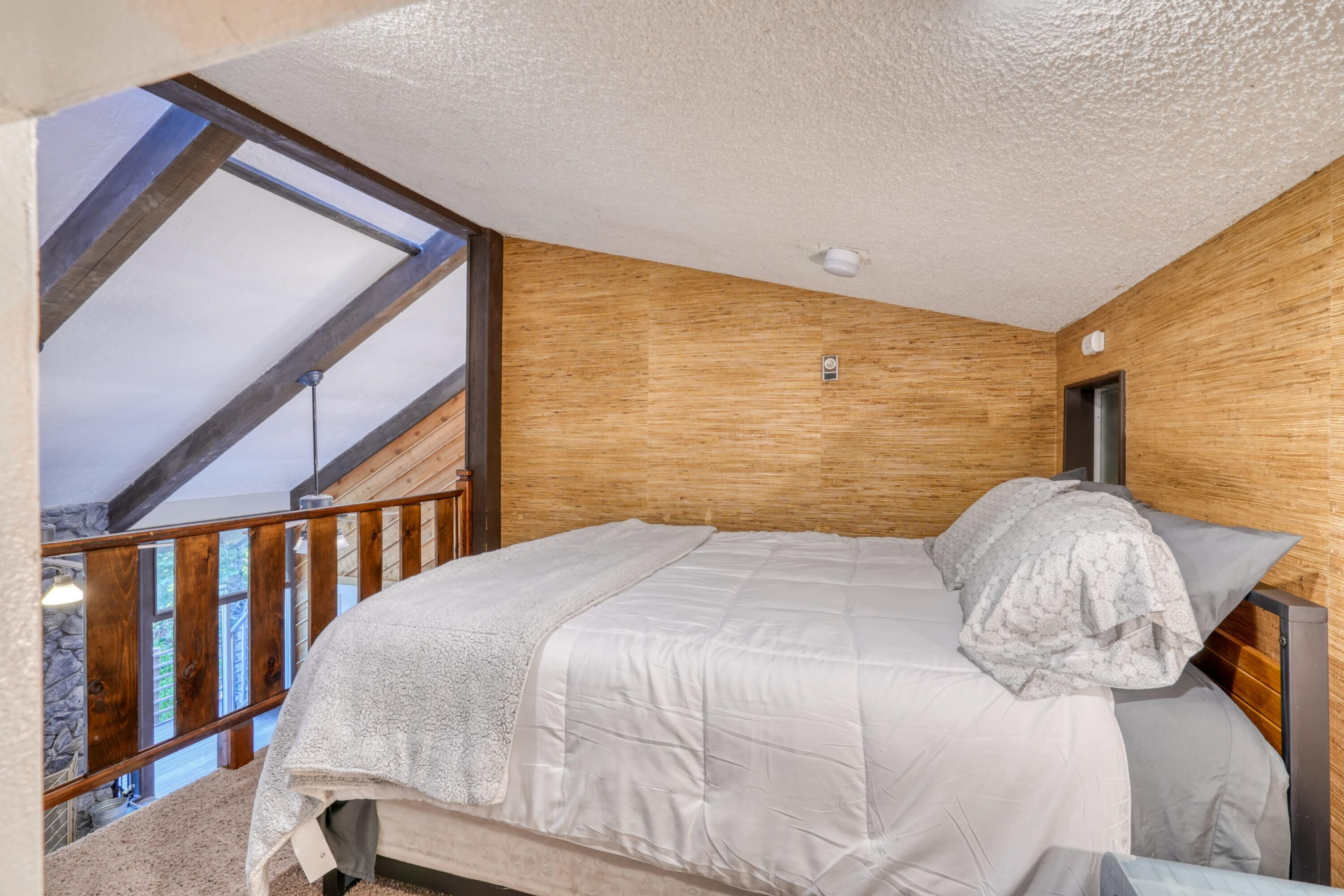 A bedroom with a wooden headboard, a bed with a white comforter, and a view of a balcony.