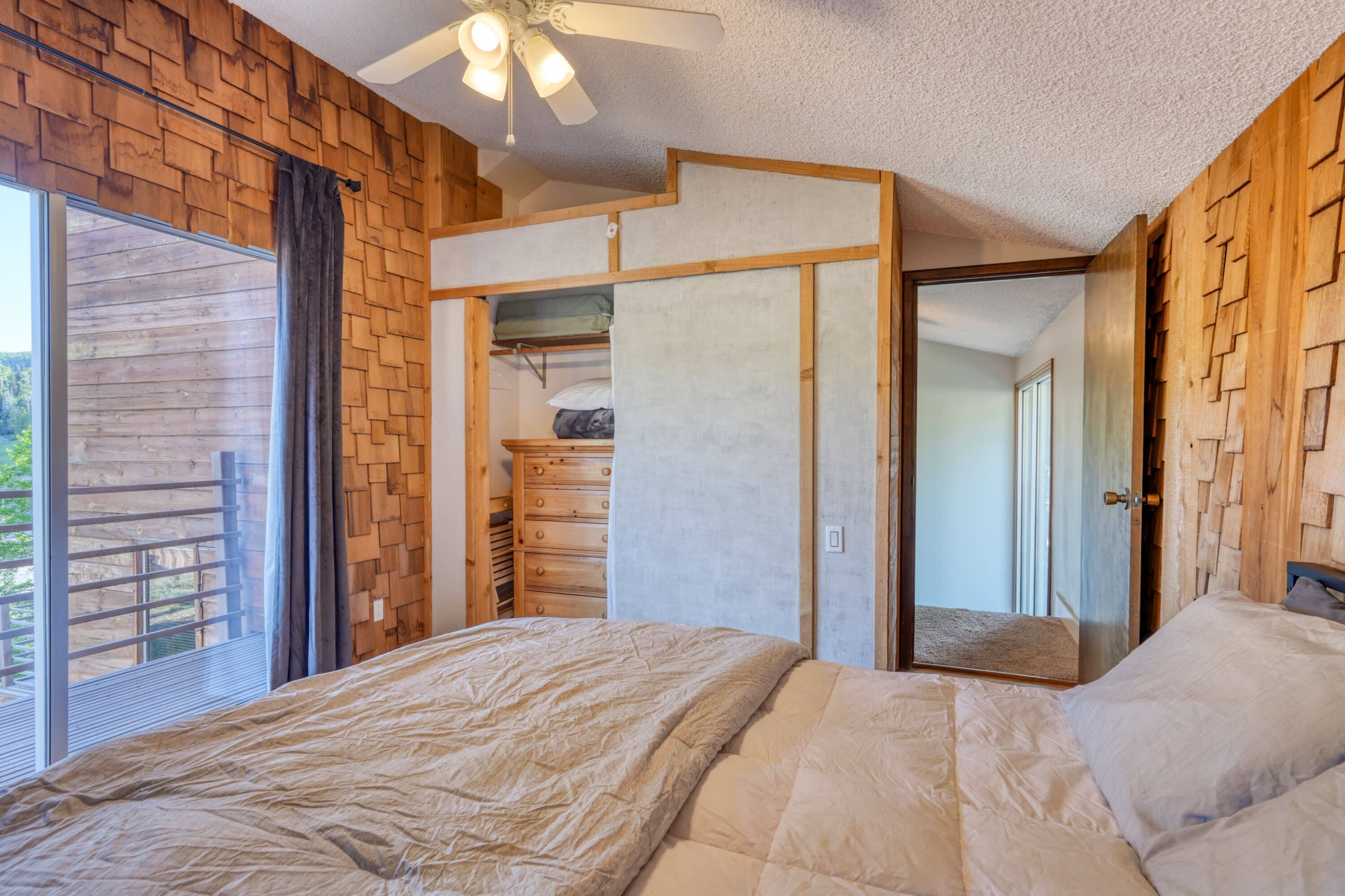 A bedroom with a bed, a ceiling fan, a wooden wall, and a sliding door leading to a closet.