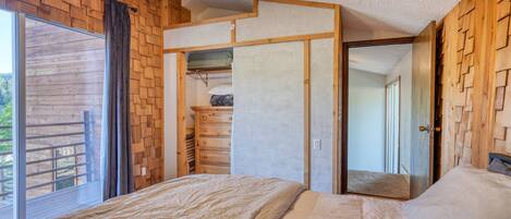 A bedroom with a bed, a ceiling fan, a wooden wall, and a sliding door leading to a closet.