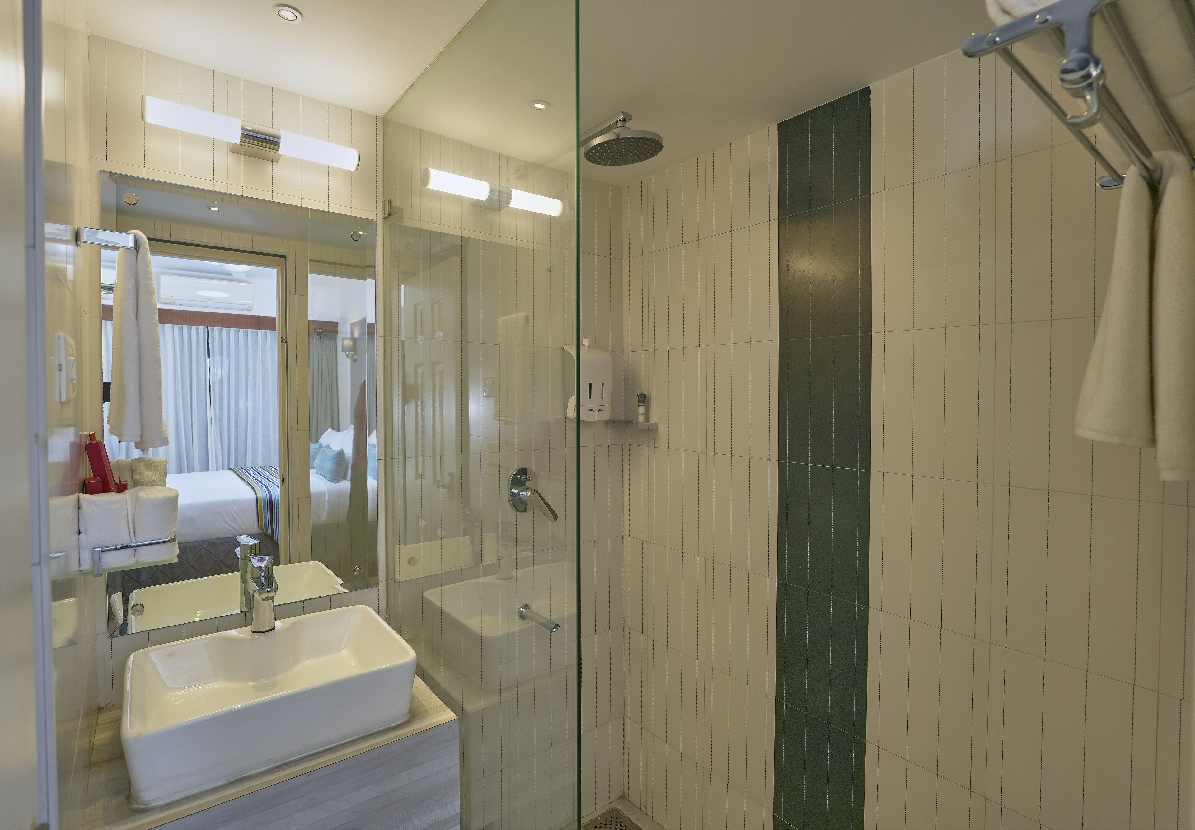 Un baño moderno con ducha envuelta en vidrio, un espejo grande y un lavabo blanco.