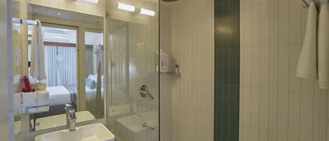 Un baño moderno con ducha envuelta en vidrio, un espejo grande y un lavabo blanco.