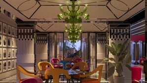 A modern dining area with a black and white striped floor, colorful chairs, and a green chandelier. - Noah Sky Suites (Aluva)