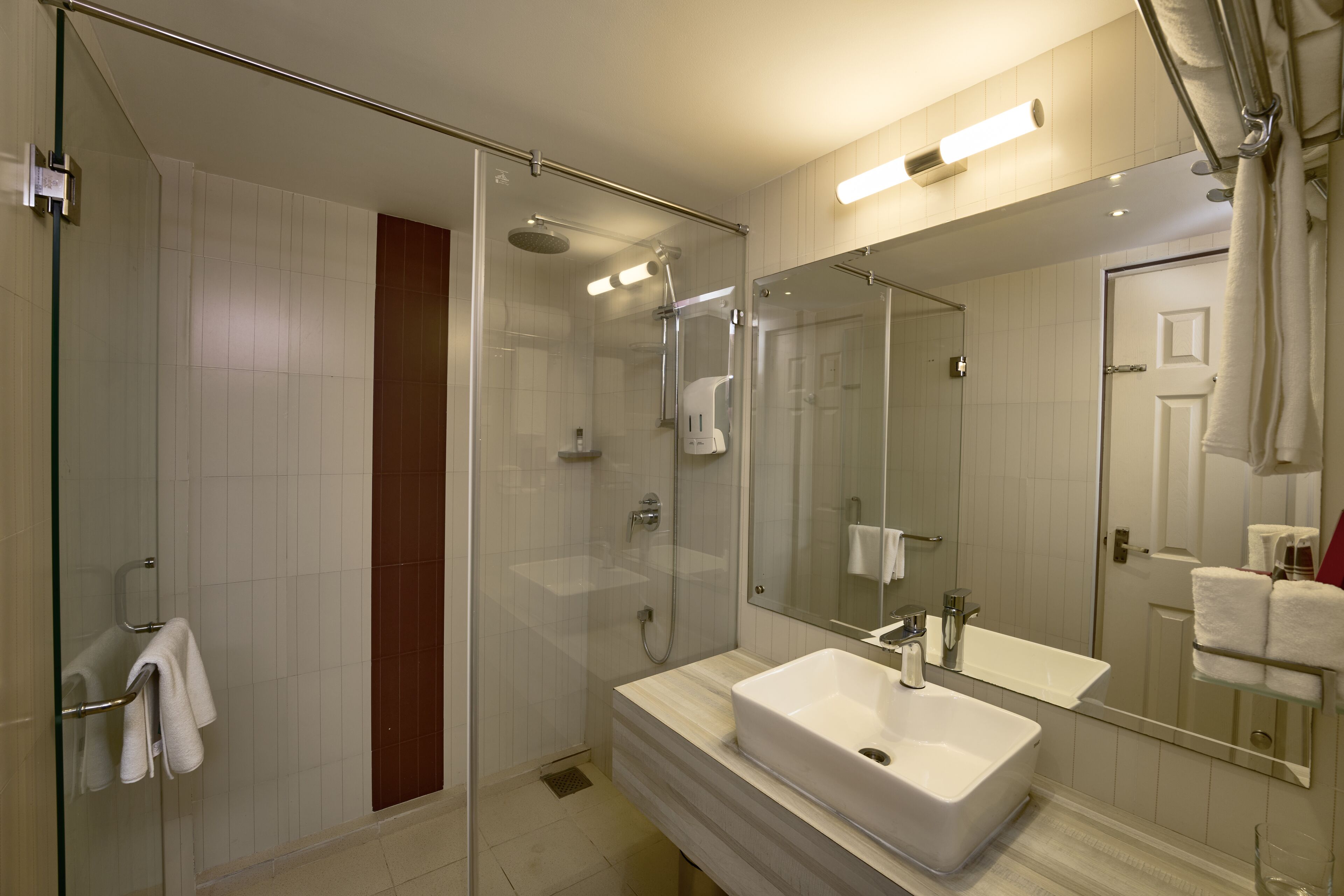 A modern bathroom with a glass-enclosed shower, a large mirror, and a white sink.