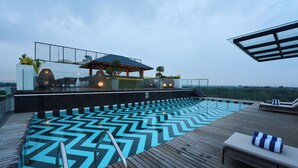 A rooftop pool with a geometric tile pattern, outdoor seating, and a bar area. - Noah Sky Suites (Aluva)