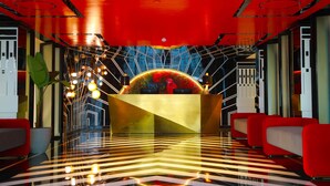 A modern lobby with a central reception desk, red seating, and a geometric patterned floor. - Noah Sky Suites (Aluva)