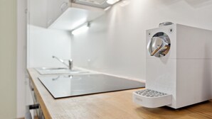 A modern kitchen with a stainless steel sink, a white countertop, and a compact, white appliance with a metallic handle. - Florian's apartments (Vienna)