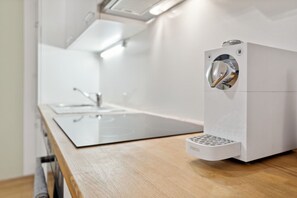 A modern kitchen with a stainless steel sink, a white countertop, and a compact, white appliance with a metallic handle.