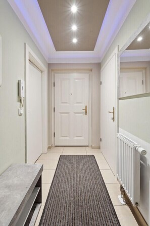 A hallway with a bench, double doors, a radiator, and a light switch on the wall.