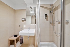 A modern bathroom with a glass-enclosed shower, a white sink, and a small wooden stool.