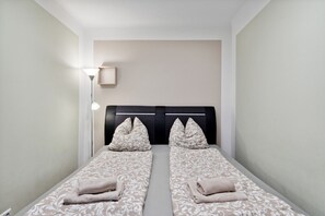 A twin room with two beds, a bedside table, a lamp, and a wall-mounted shelf.