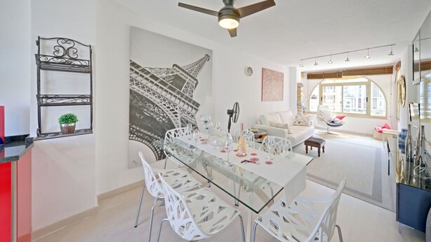 A modern dining area with a glass table, white chairs, and a ceiling fan.