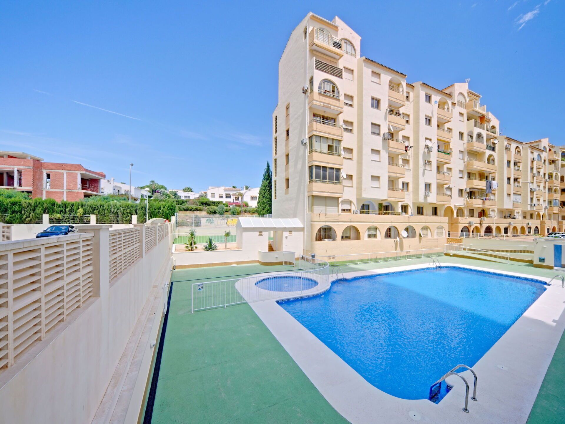 A swimming pool adjacent to a multi-story residential building with balconies and a green lawn area.