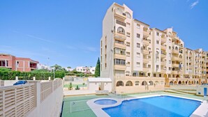 A swimming pool adjacent to a multi-story residential building with balconies and a green lawn area.