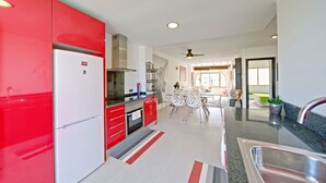 A modern kitchen with red cabinets, a white refrigerator, and a dining area with a striped rug.