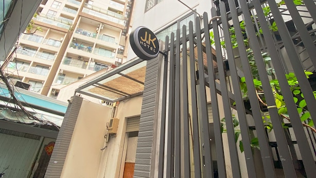Entrada de un hotel con un letrero que dice "JK Hotel", un acceso mediante un portón y una escalera que lleva al edificio.
