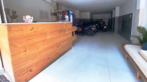 Zona de recepción con mostrador de madera, un refrigerador de Pepsi y una motocicleta estacionada al fondo.
