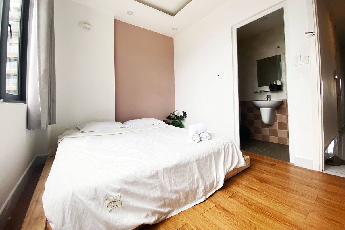 A bedroom with a bed, a plant, and a bathroom visible through an open door.
