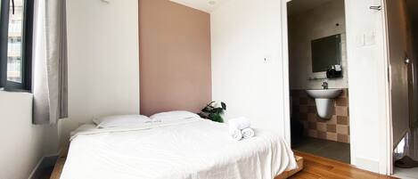 A bedroom with a bed, a plant, and a bathroom visible through an open door.
