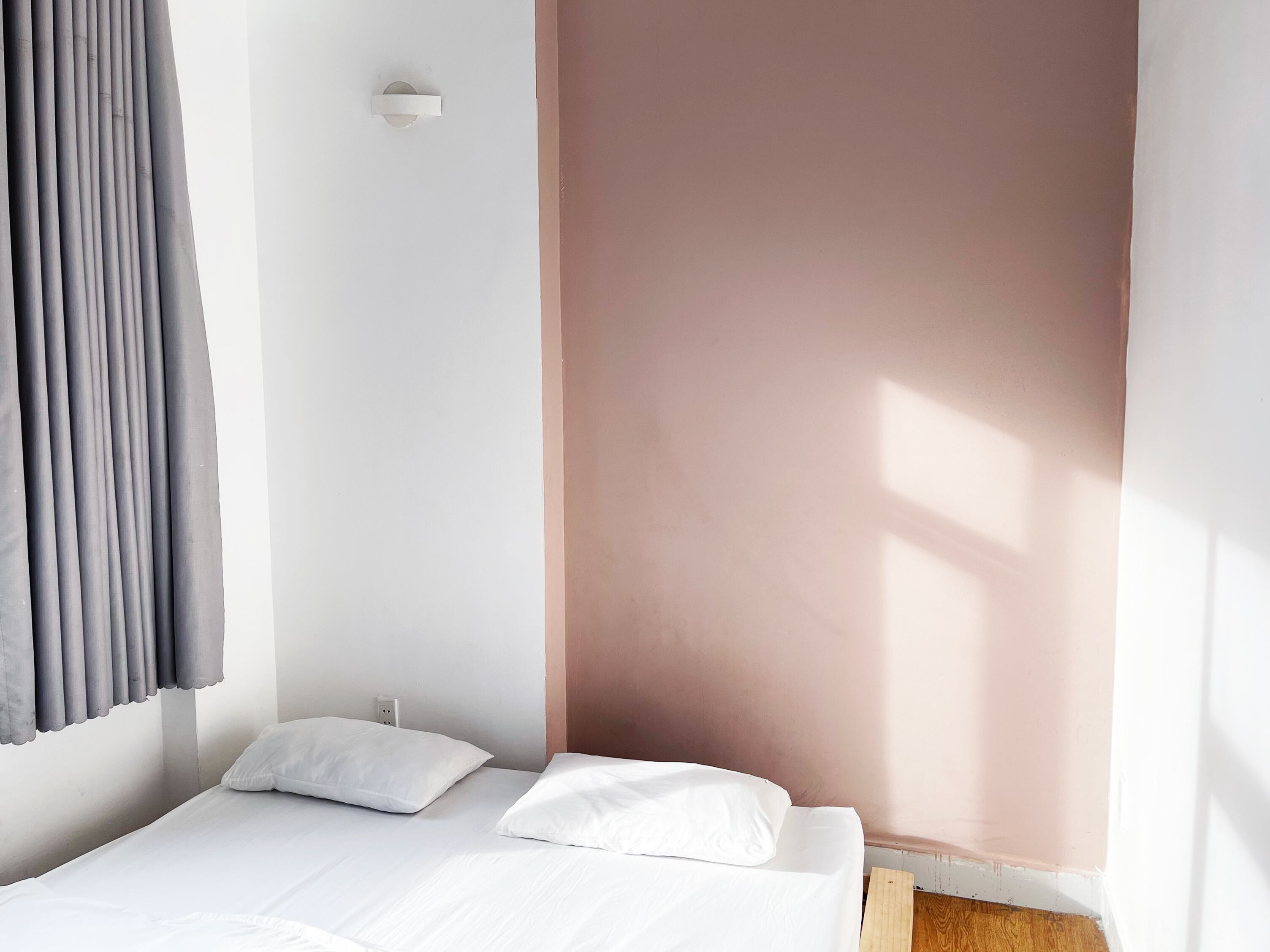 Een minimalistische slaapkamer met een enkel bed, wit beddengoed en een raam met natuurlijk licht.