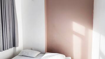 Een minimalistische slaapkamer met een enkel bed, wit beddengoed en een raam met natuurlijk licht.