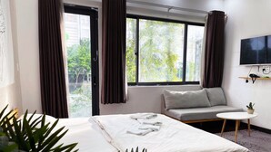 Habitación de hotel con cama, sofá, mesita, televisor y ventana con cortinas.