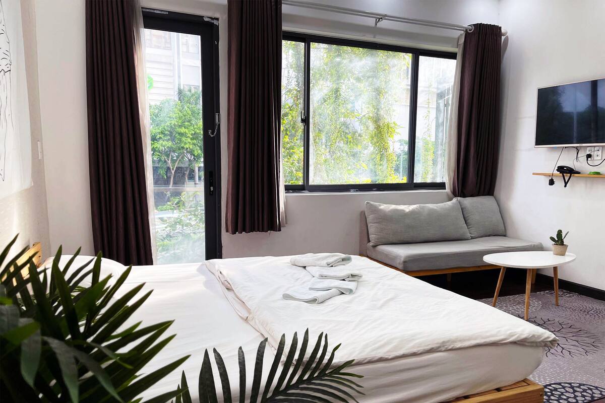 A hotel room with a bed, a sofa, a small table, a TV, and a window with curtains.