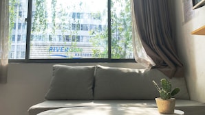 Una habitación con sofá, una mesita y una ventana con vistas a un edificio que dice "RIVERCORE RESIDEN".