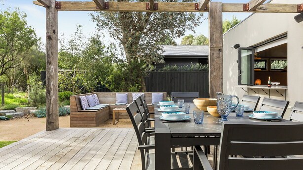 Eine Holzterrasse mit integriertem Sitz eine Tisch gedeckt mit Tellern und Gläsern sowie einer Pergola.