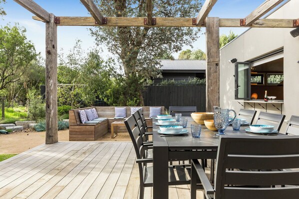 A wooden deck with a built-in bench, a table set with plates and glasses, and a pergola structure.