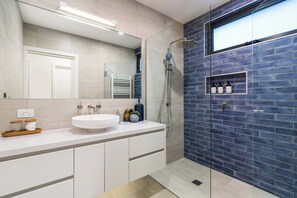 A modern bathroom with a white sink, a glass-enclosed shower, and a blue-tiled wall.