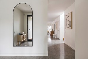 A hallway with a mirrored wall, a wooden cabinet, and a door leading to another room.
