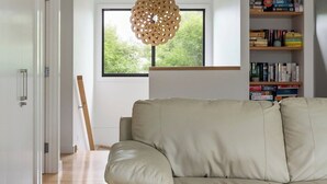 Een moderne woonkamer met een bank, een boekenkast en een raam met uitzicht op groen.