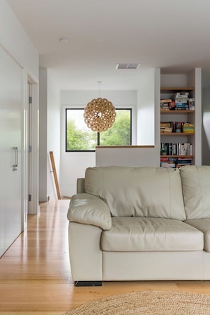 En moderne stue med sofa, bogreol og et vindue med udsigt til grønne omgivelser.