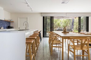 A modern kitchen with a central island, a dining area with wooden chairs, and large sliding glass doors leading to an outdoor patio.
