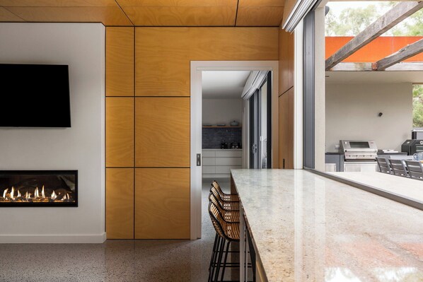 A modern kitchen with a large island, a fireplace, and a view of the outdoor area.