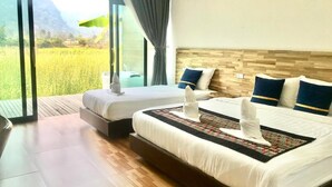 A hotel room with two beds, a large window with curtains, and a view of a green landscape.