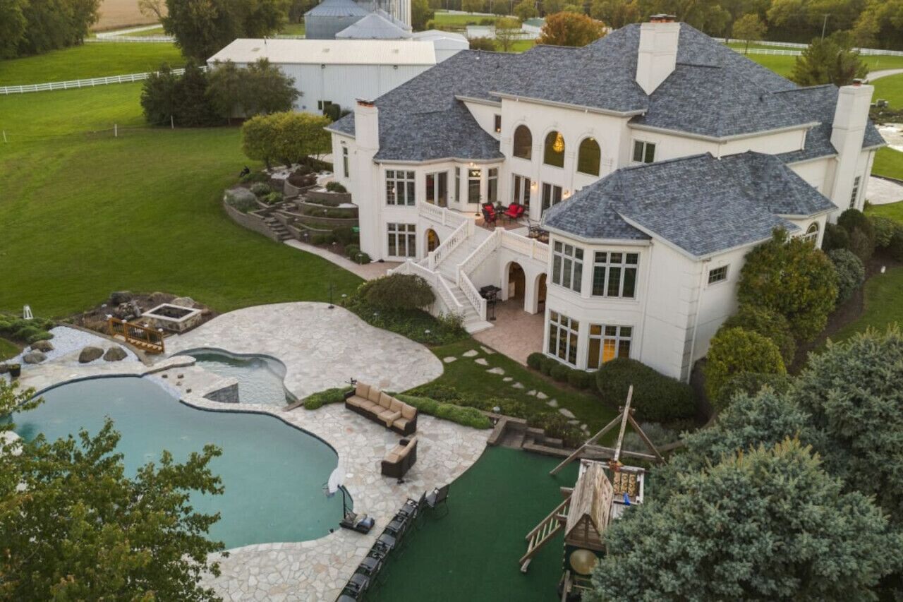 A large, white mansion with a swimming pool, a covered patio, and a well-maintained lawn.