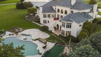 A large, white mansion with a swimming pool, a covered patio, and a well-maintained lawn.
