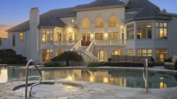 Una casa grande y elegante con piscina, un patio cubierto y una imponente escalera que conduce a la entrada.