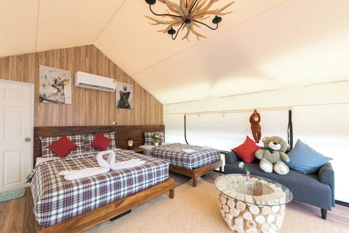 Une chambre avec deux lits, un canapé, une table basse ronde en verre et un plafond en bois.