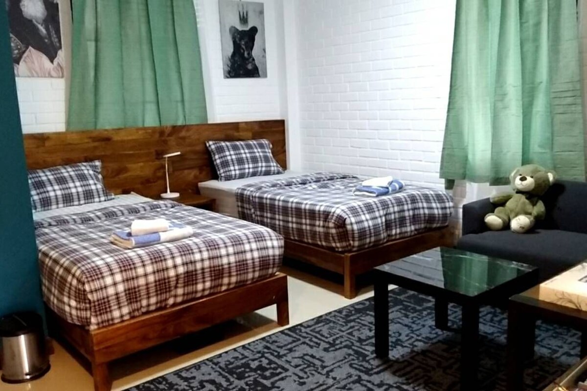 Ein Zimmer mit zwei Holzbett, einem Glastisch, einer Couch und einem Teddybären.